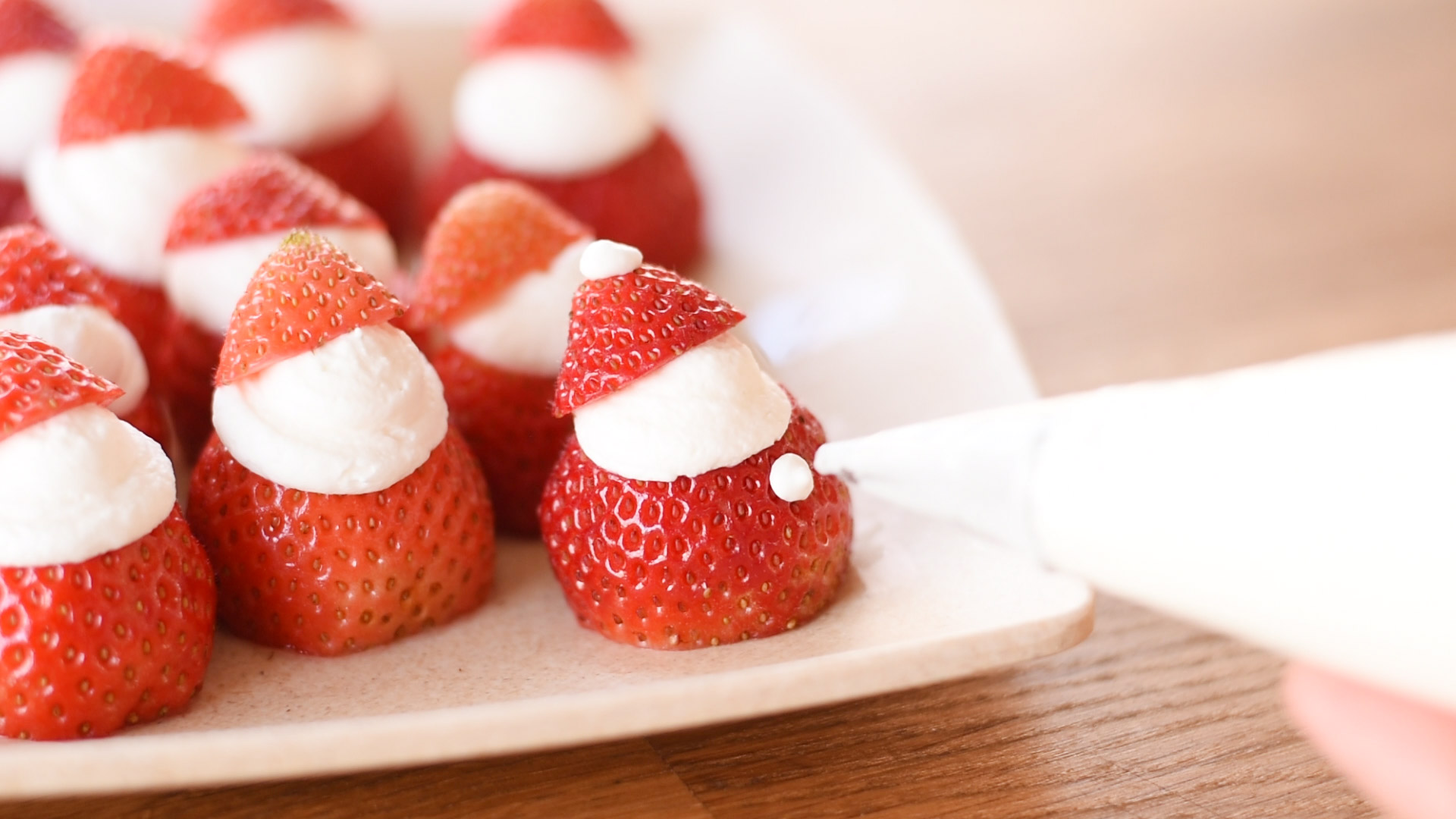 Strawberry Santas being decorated with whipped cream buttons.